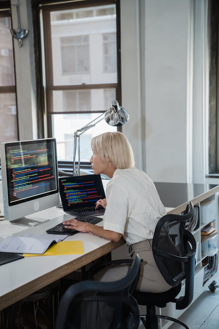 Home Blonde woman coding at desk with dual monitors in a contemporary office.